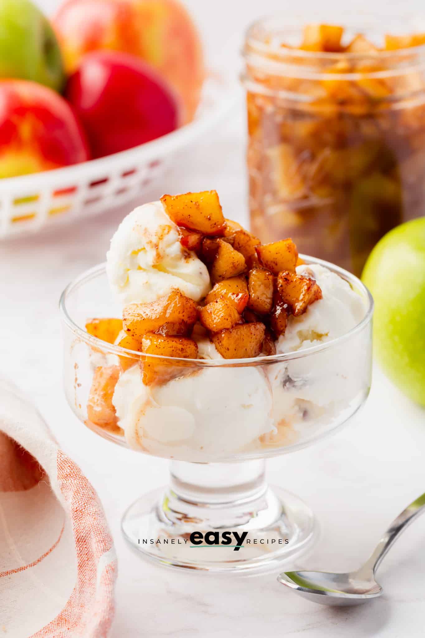 white ice cream in a glass jar with brown apple diced on top with apples in the background