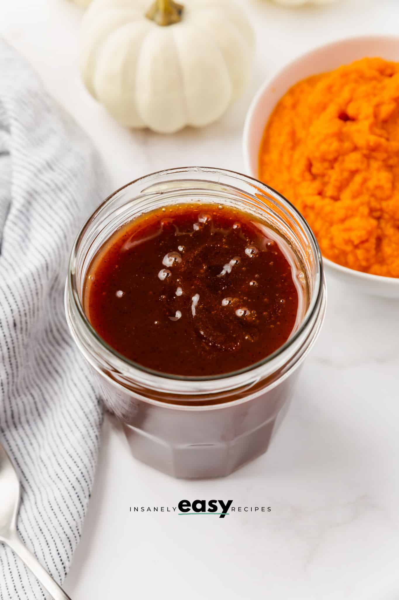 glass jar with brown liquid in it, pumpkin puree to top right in a white bowl