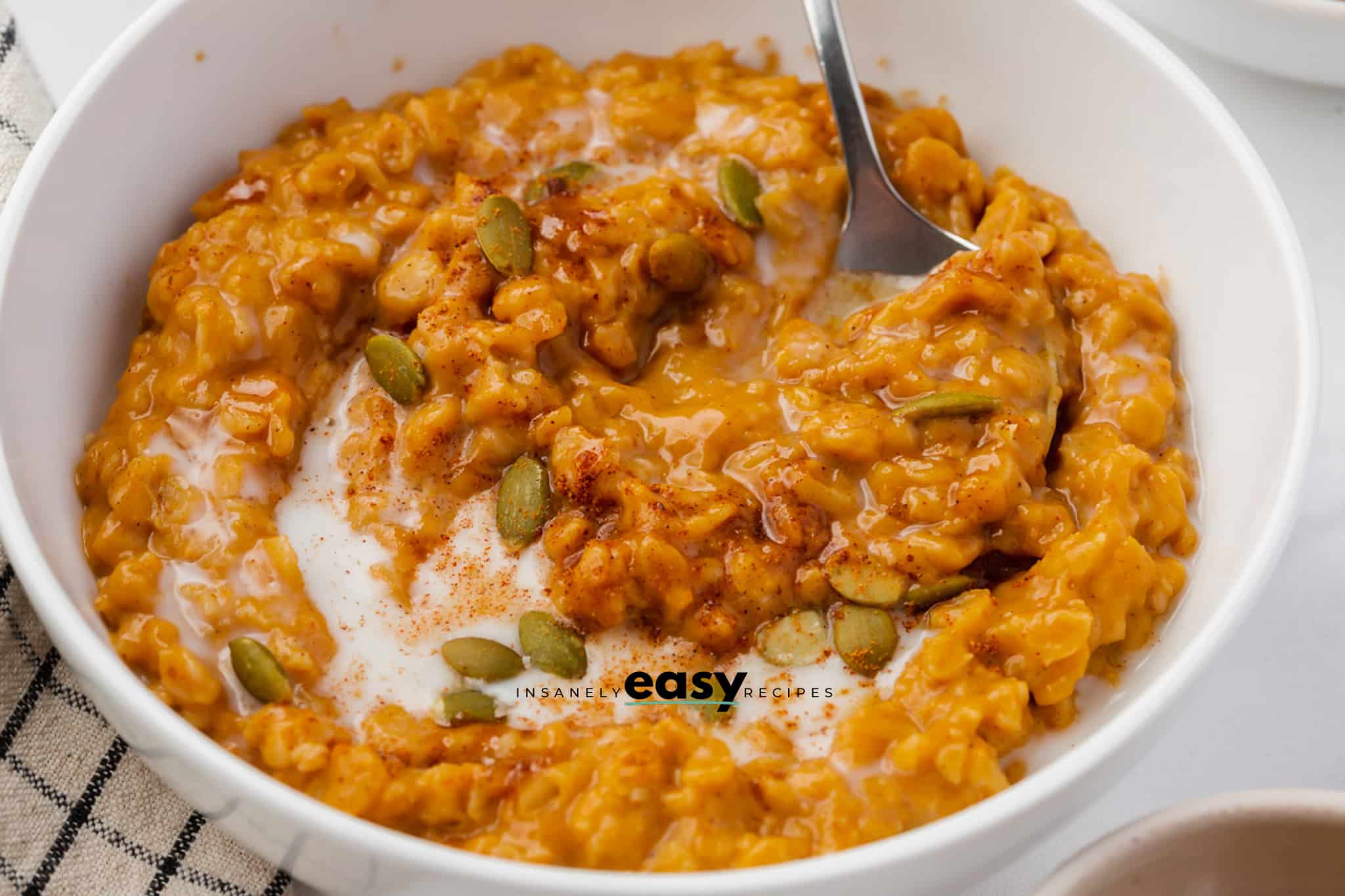 Closeup of pumpkin oatmeal with cream, cinnamon, and green pumpkin seeds.