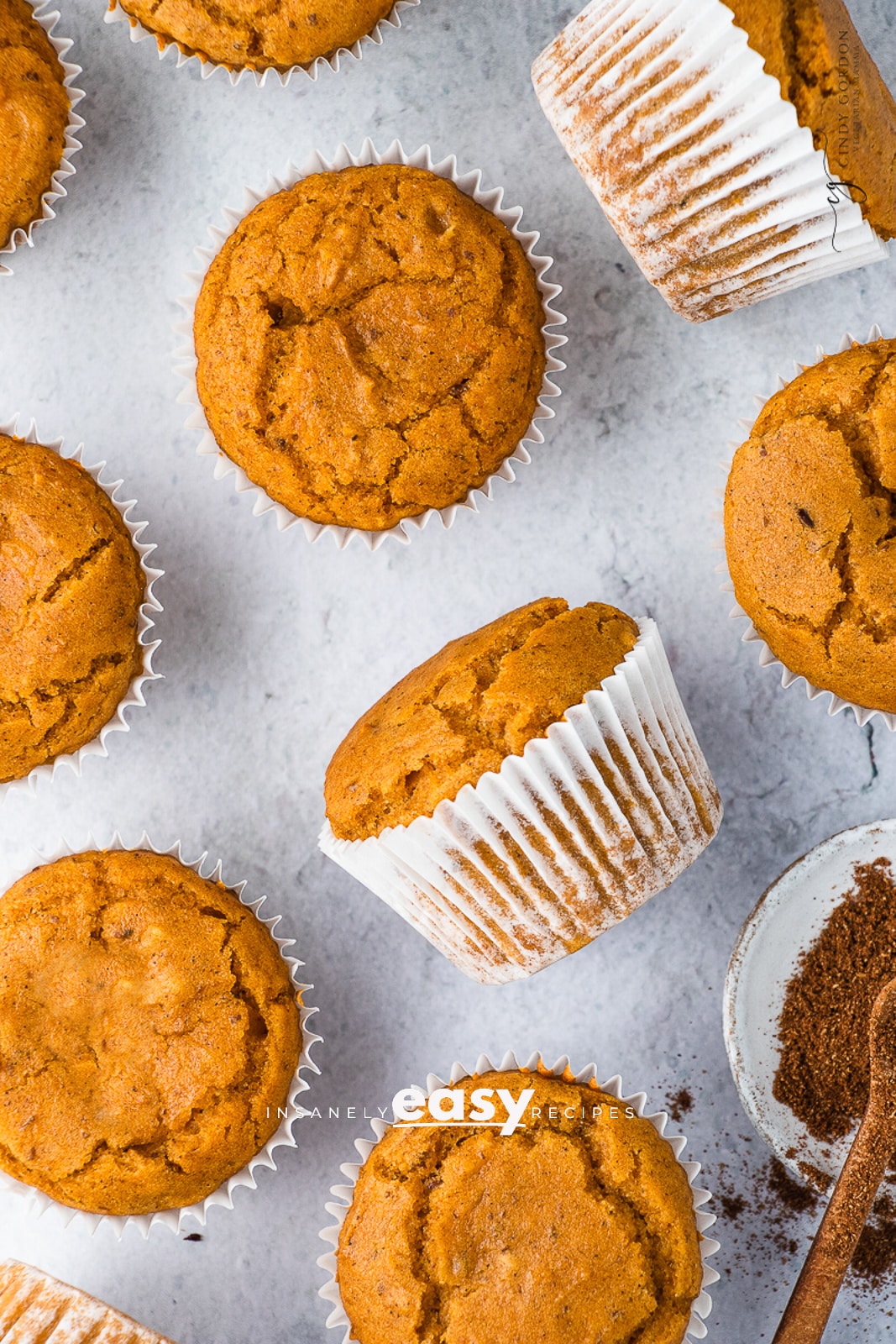 Closeup photo of multiple Vegan Pumpkin Muffins and a dish with pumpkin spice in the bottom corner