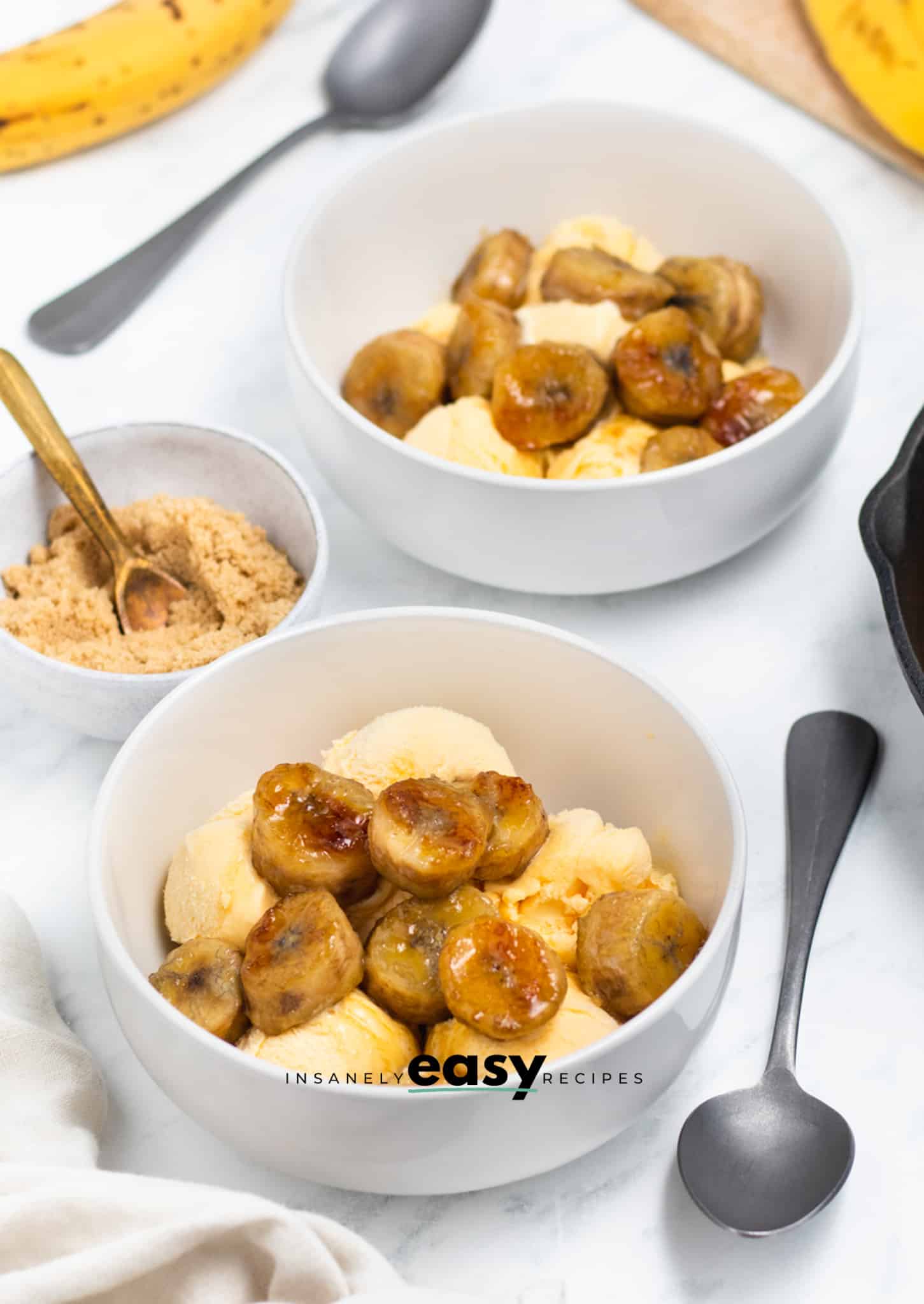 Photo of two white bowls filled with vanilla ice cream with caramelized bananas on top. 