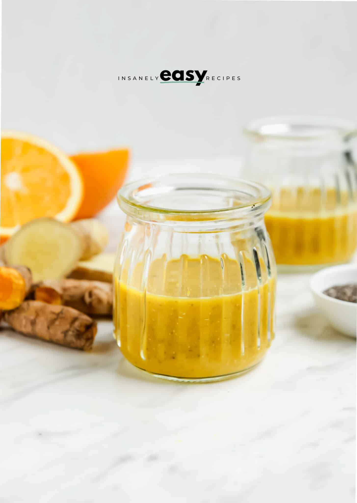 Closeup photo of a Wellness Shot, consisting of orange juice, fresh turmeric, and chia seeds, in a small glass cup. 