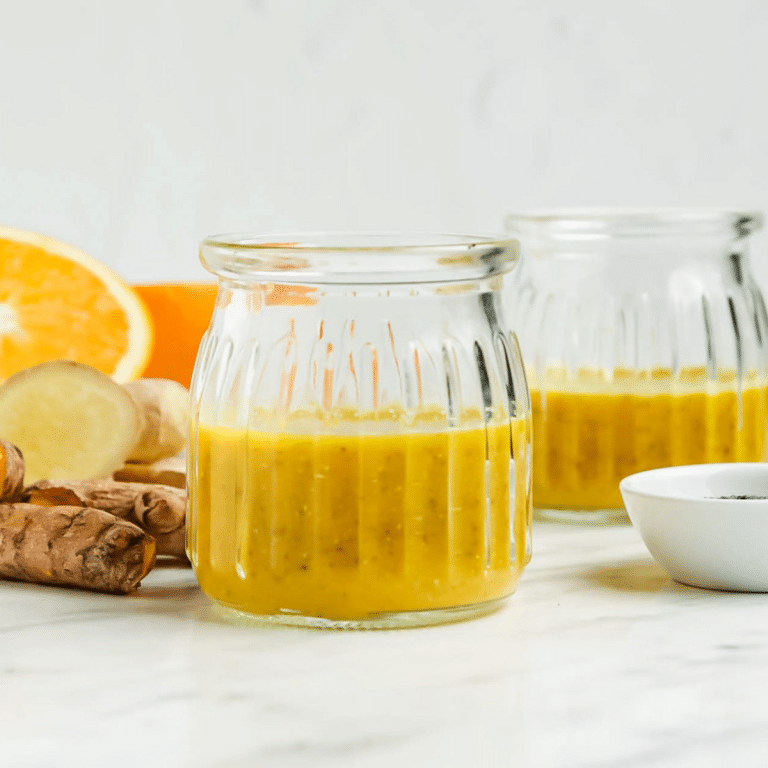 Closeup photo of a Wellness Shot, consisting of orange juice, fresh turmeric, and chia seeds, in a small glass cup.