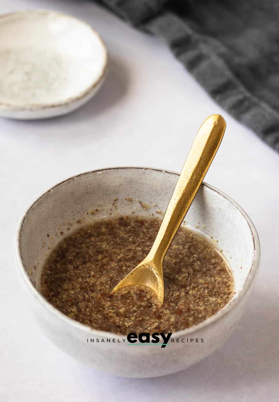 Photo of a white bowl with a flax egg in the bowl. There is a golden spoon in the bowl.