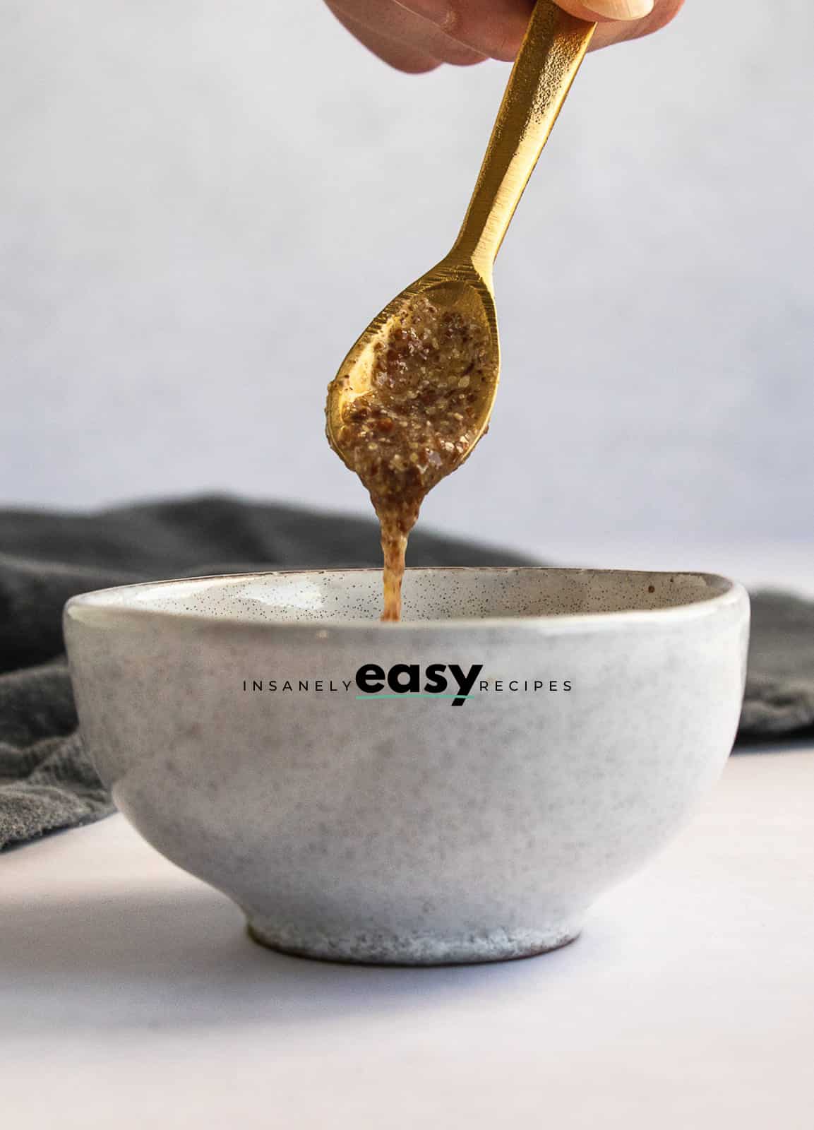 Photo of a white bowl with a flax egg in the bowl. There is a golden spoon with a spoonful of flax egg in the spoon.