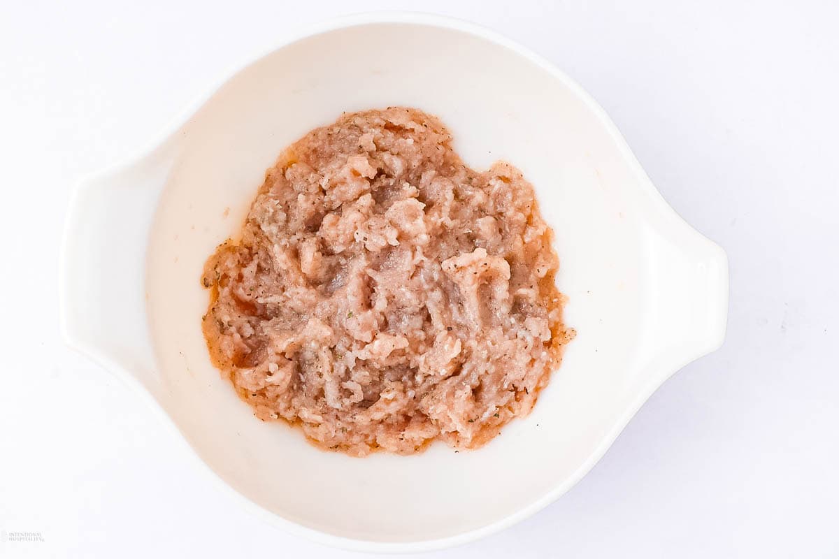 A white bowl containing raw ground turkey. The meat is light pink with a slightly coarse texture, spread across the bottom of the bowl. The background is a plain white surface.