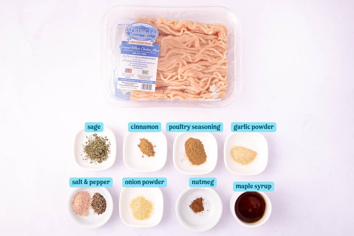 Top-down view of ingredients for a recipe. Includes a pack of ground chicken and nine small dishes containing sage, cinnamon, poultry seasoning, garlic powder, salt & pepper, onion powder, nutmeg, and maple syrup.