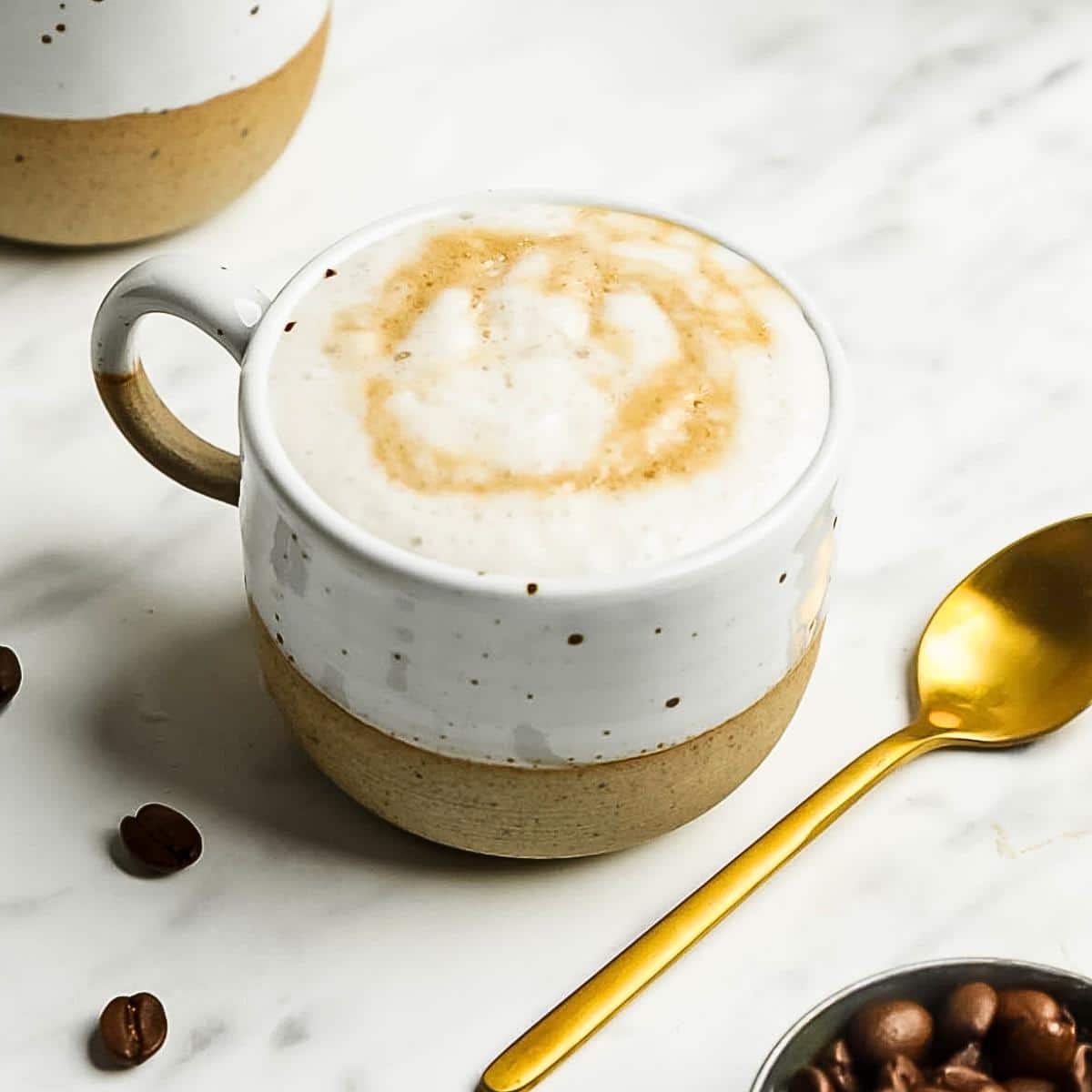 Oat milk latte in a cup sprinkled with some cinnamon powder on top, few coffee beans on the side