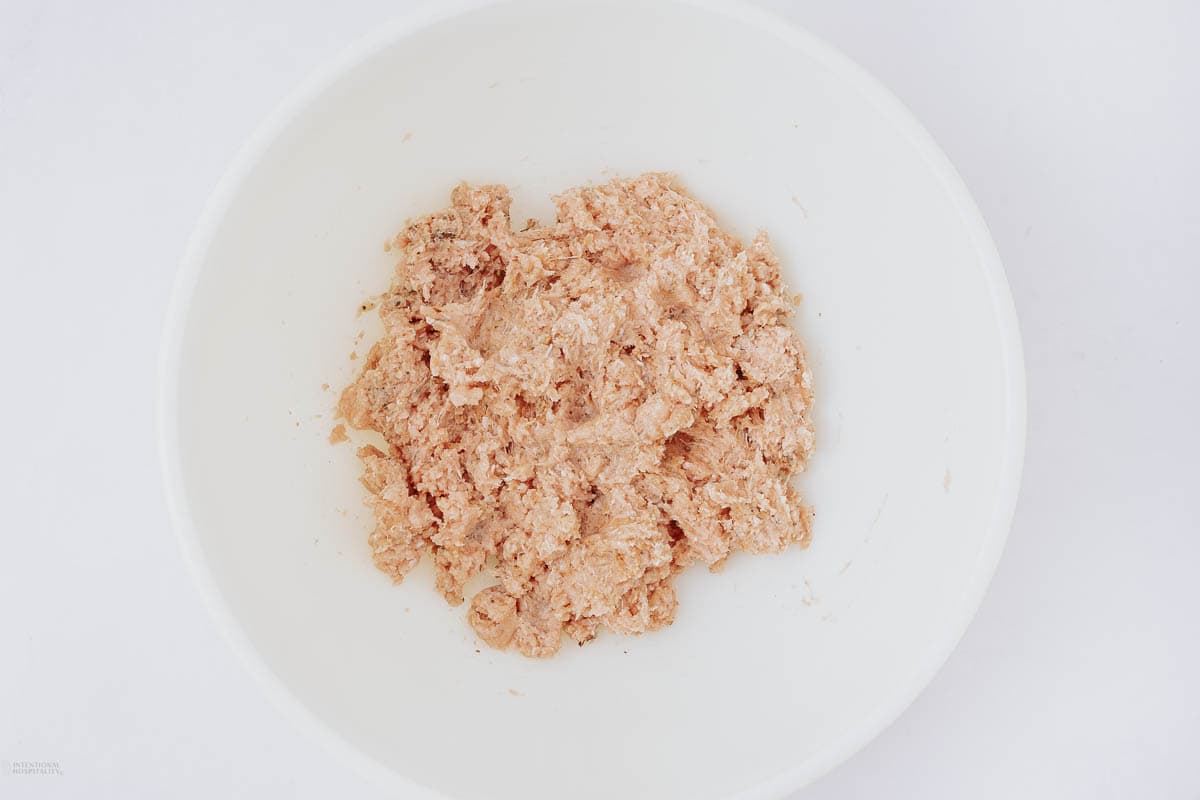 A white bowl containing a spread of blended light pinkish-beige mixture, resembling ground meat or a meat paste, set against a plain white background.