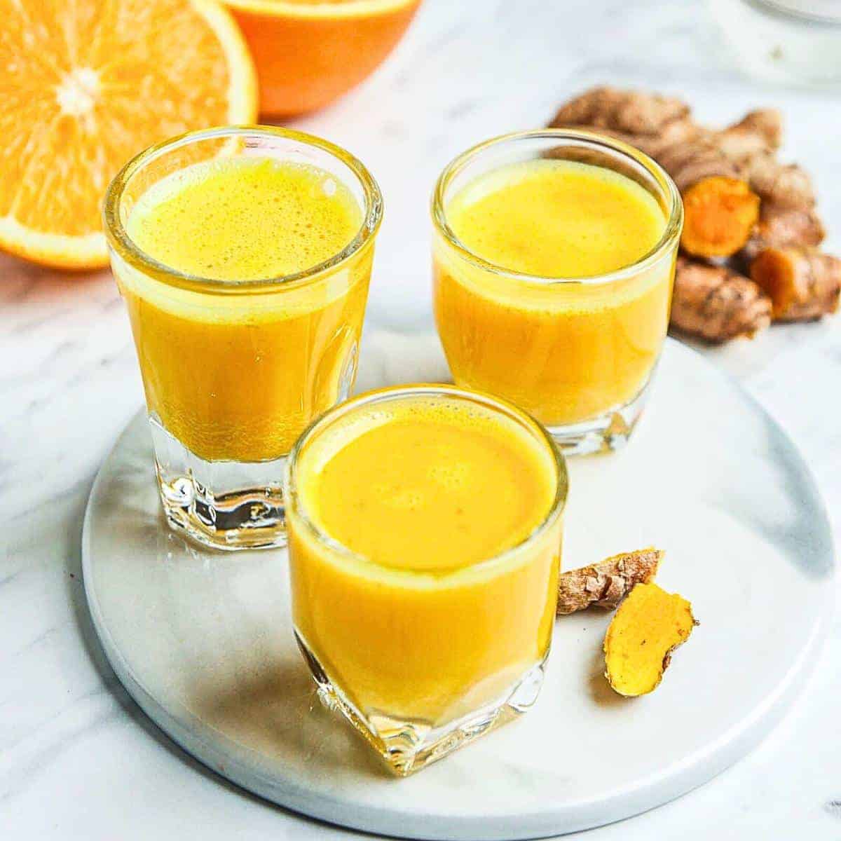 Turmeric shot in shot glasses, fresh turmeric and oranges nearby