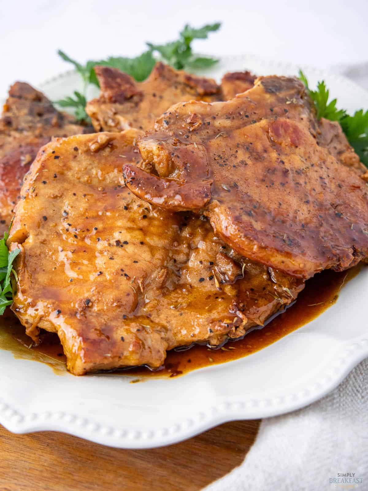 Close-up of glazed pork chops garnished with herbs, served on a white plate. The chops are seasoned and have a rich, brown sauce, adding a glossy texture.