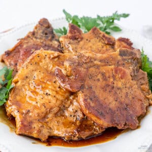 Cooked pork chops drizzled with a savory glaze, served on a white plate with a garnish of fresh parsley.