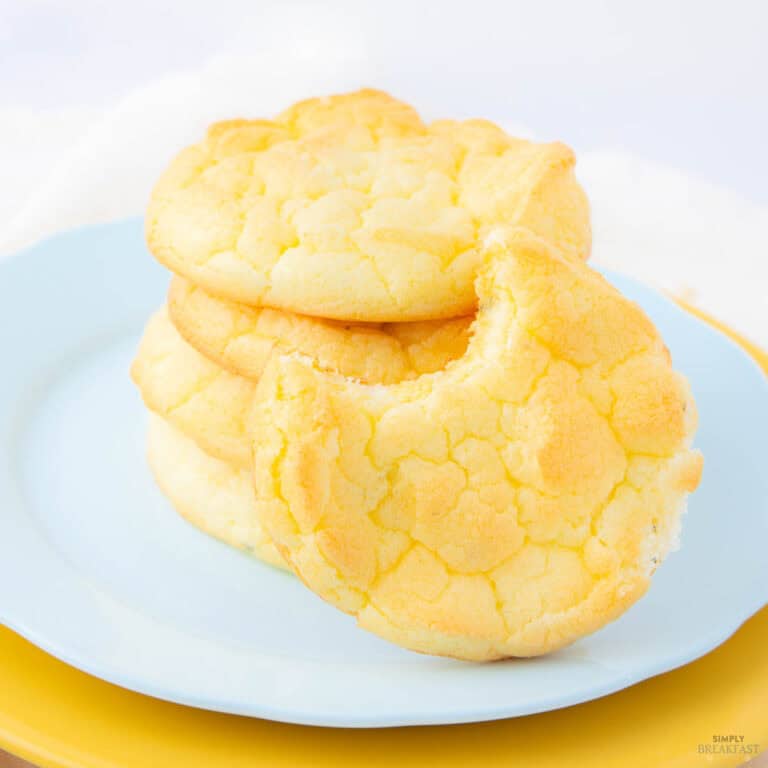 A stack of golden-brown cookies on a light blue plate. The top cookie has a bite taken out of it, revealing a soft texture. The background is bright and out of focus, highlighting the cookies.