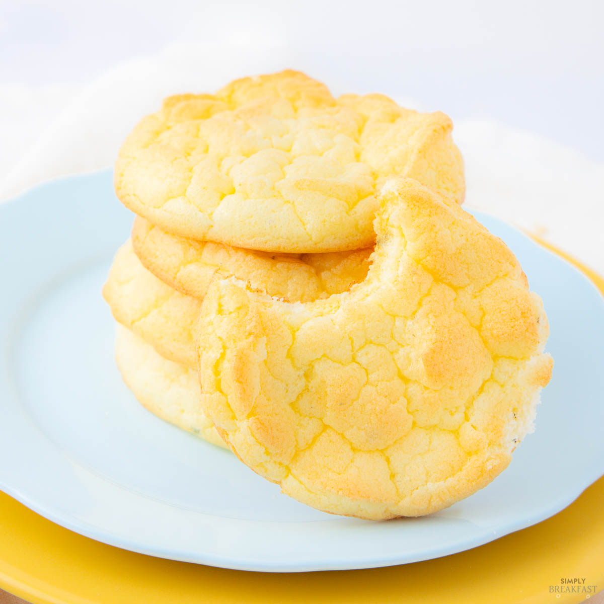 yellow cloud bread stacked on a blue plate, with one bitten piece