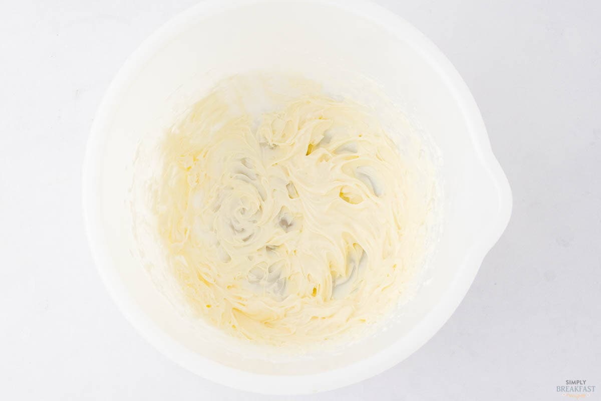 A white bowl filled with smooth, creamy butter, light in color, against a white background. The butter appears to have been whipped, with visible swirls and peaks.