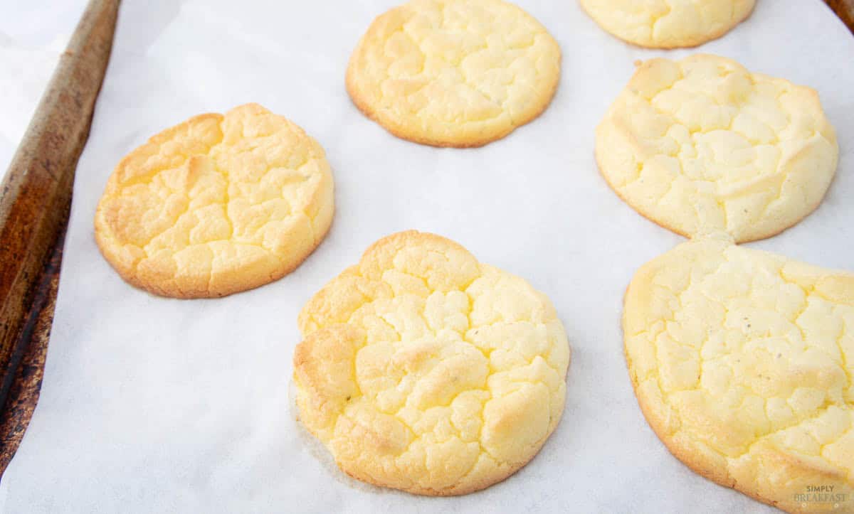 Freshly baked cookies with a cracked golden top rest on parchment paper on a baking sheet.