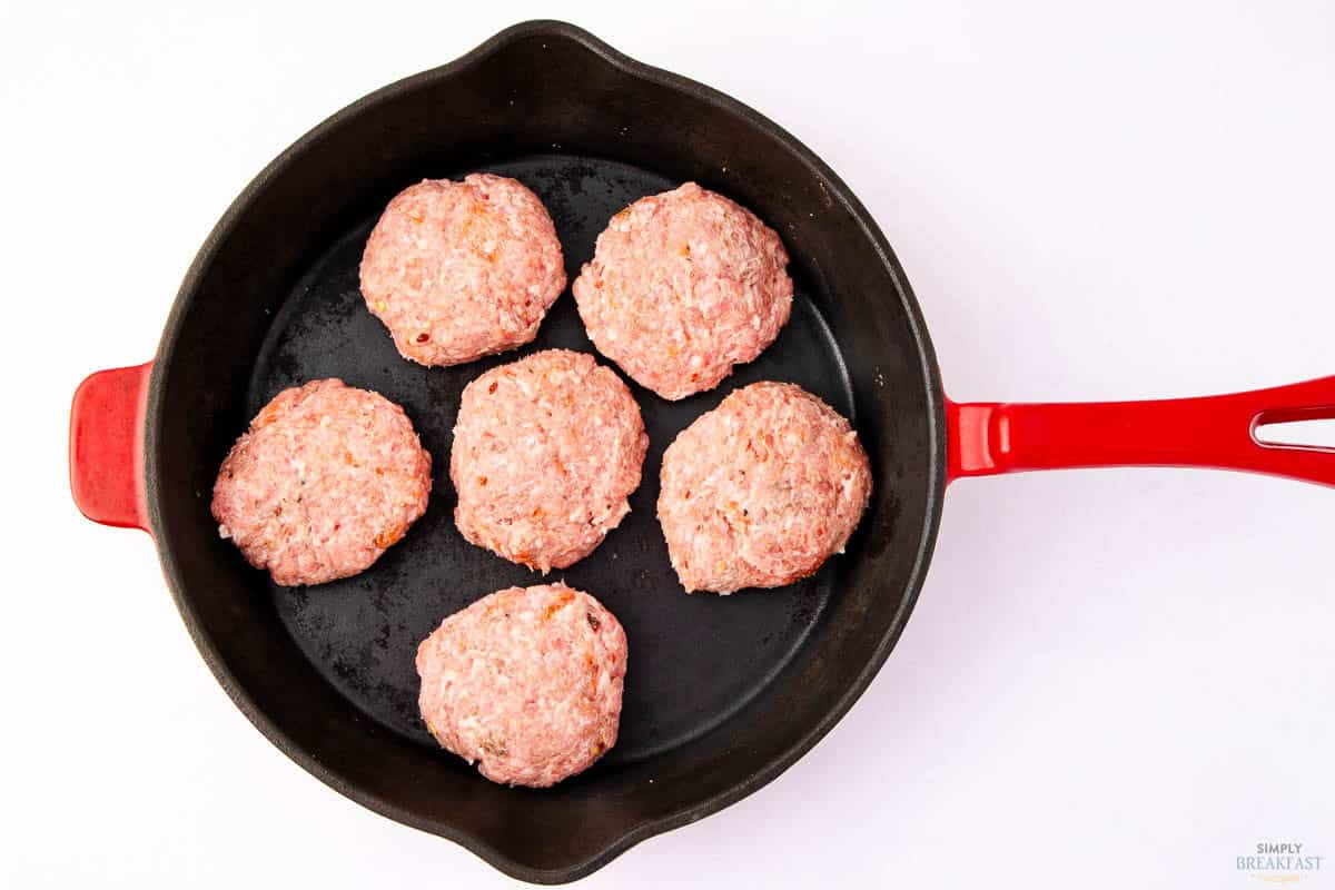 Red-handled pan with six raw ground meat patties evenly spaced inside, placed against a white background.