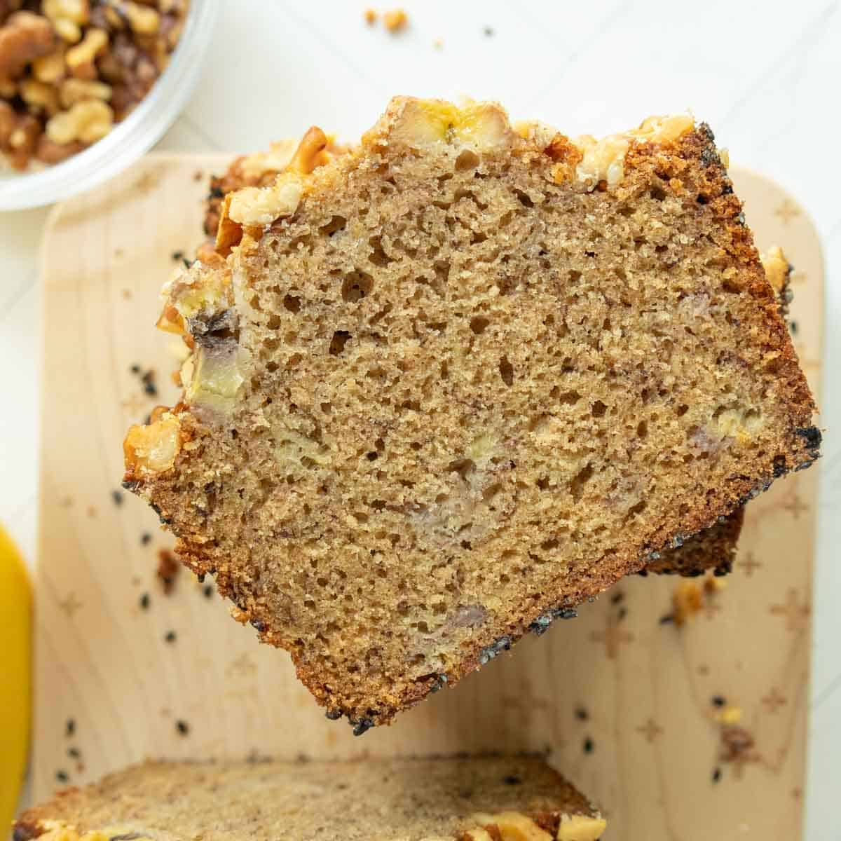 A slice of banana bread stacked on other slices, sitting on a wooden cutting board.