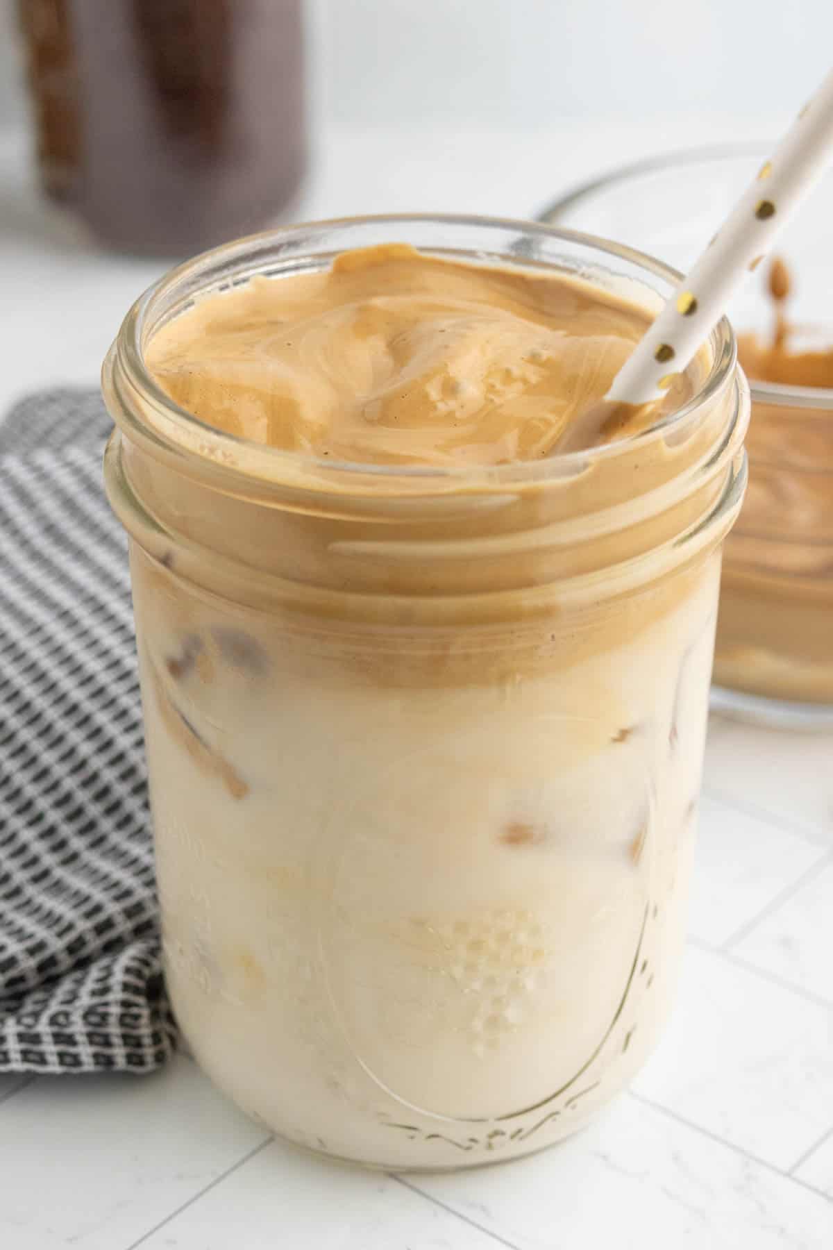 A glass jar filled with milk and whipped coffee that are slightly mixed.