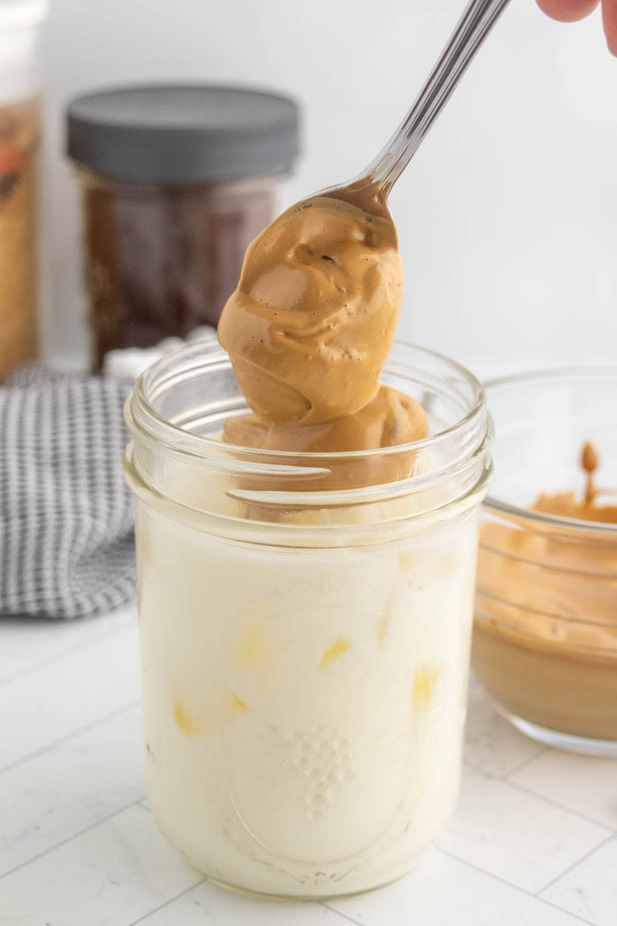 Whipped coffee being spooned onto milk in a glass jar.