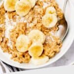 Bowl of oatmeal topped with banana slices and a sprinkle of cinnamon, with a spoon on the side.
