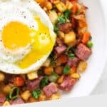 A plate of corned beef hash with diced potatoes, carrots, and green onions, topped with a sunny-side-up egg.