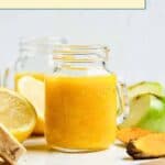 A mason jar filled with yellow ginger turmeric juice sits on a counter, surrounded by lemon, ginger, and turmeric roots.