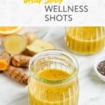 Two small glass jars filled with yellow chia seed wellness shots, with ginger, turmeric roots, orange slices, and chia seeds on a marble surface. Text reads "Chia Seed Wellness Shots.