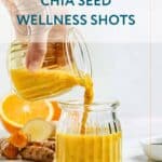 A hand pours a yellow chia seed wellness shot from a small jar into a glass, with oranges and turmeric on the counter.