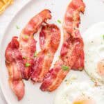 Slices of cooked bacon on a plate with eggs.