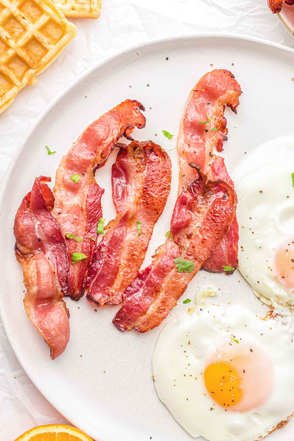 Slices of cooked bacon on a plate with eggs.