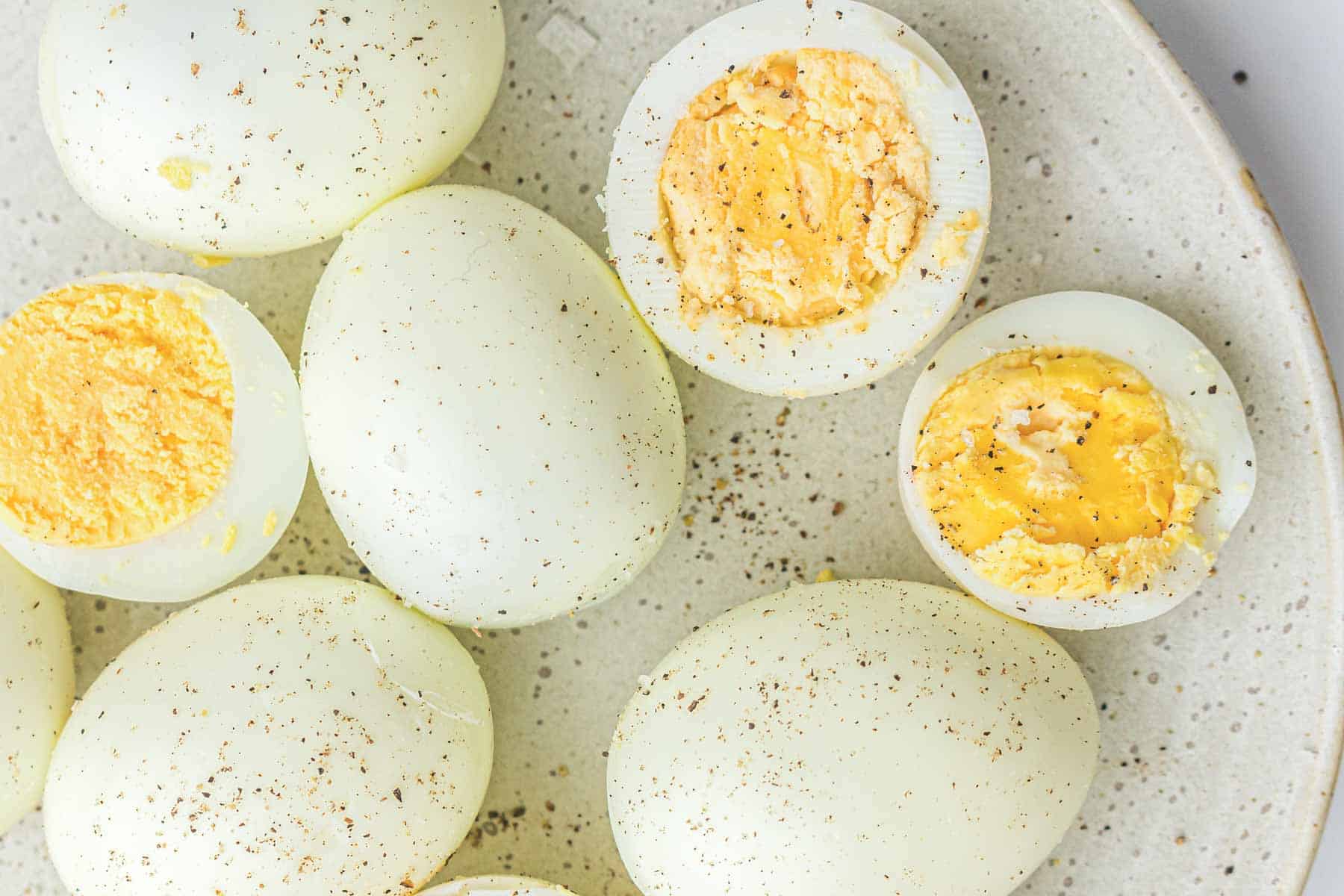 A plate of air fryer hard boiled eggs, some whole and some cut in half, seasoned with ground black pepper.