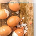 Several brown eggs, some partially peeled, rest on a wooden cutting board. Eggshell fragments are scattered around. Text above reads “Air Fryer Hard Boiled Eggs.”.