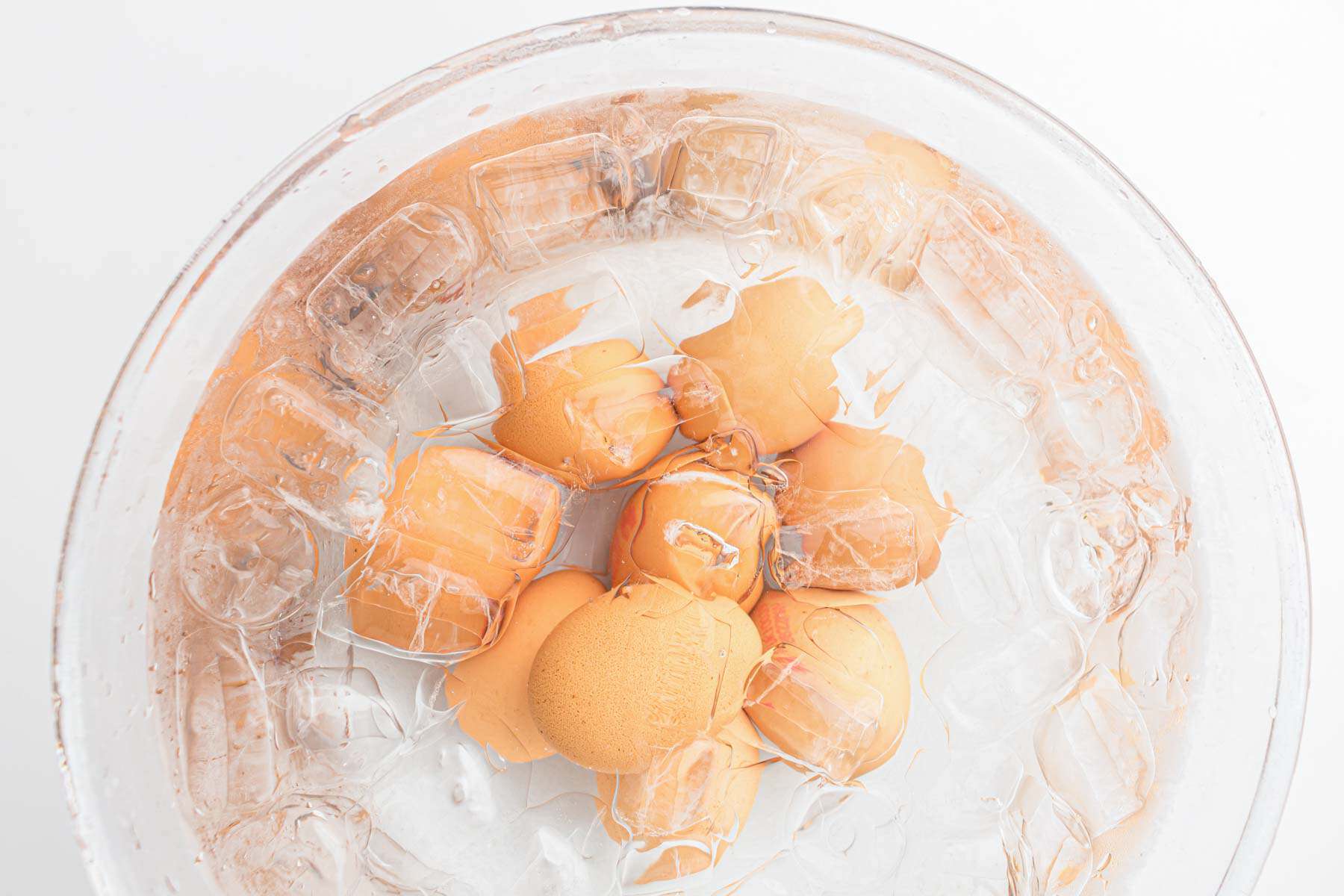Brown eggs, freshly made as air fryer hard boiled eggs, are submerged in a glass bowl filled with ice water and ice cubes, viewed from above.