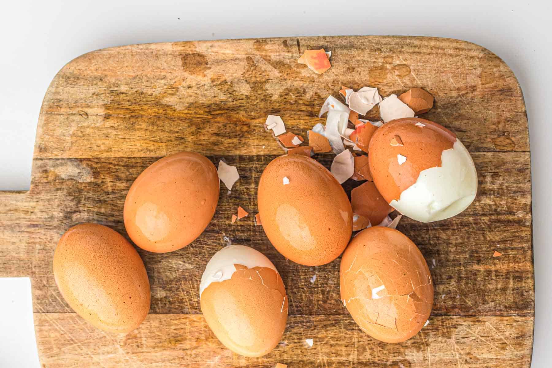Six brown eggs, some partially peeled, and eggshell fragments on a wooden cutting board—perfect for showcasing the convenience of air fryer hard boiled eggs.