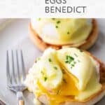Two halves of an English muffin topped with poached eggs, creamy hollandaise sauce, and fresh chives—a classic eggs benedict—served on a plate with a fork.