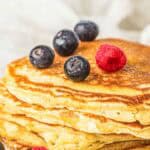 A stack of golden sourdough discard pancakes topped with fresh blueberries and raspberries on a white plate.