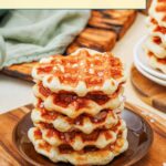 A stack of golden-brown Liege waffles sits on a brown plate, topped with coarse sugar, with more waffles and a green napkin in the background.