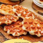 Golden brown Liege waffles with sprinkled sugar pearls are arranged on a wooden board, with more waffles and a bowl of chocolate sauce in the background. Text overlay promotes a recipe website.