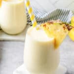 Two stemless wine glasses filled with pineapple smoothie, garnished with pineapple slices.