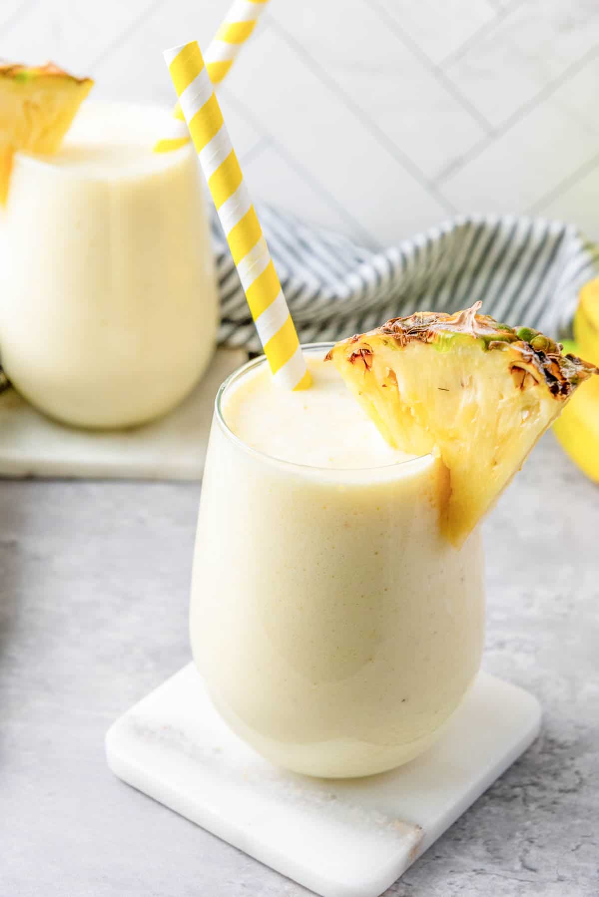 Two stemless wine glasses filled with pineapple smoothie, garnished with pineapple slices.
