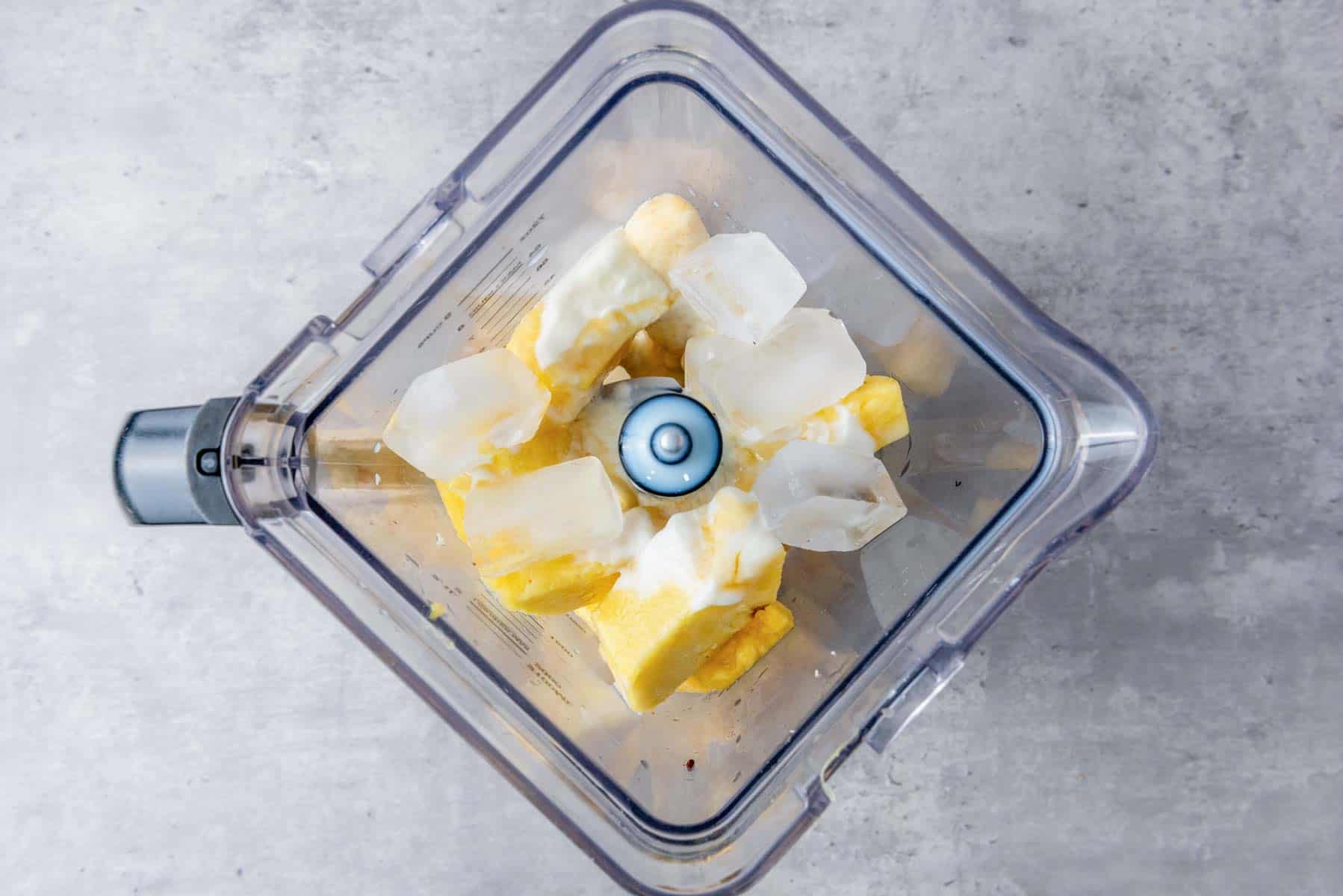 A blender with pineapple, banana, ice, and milk.