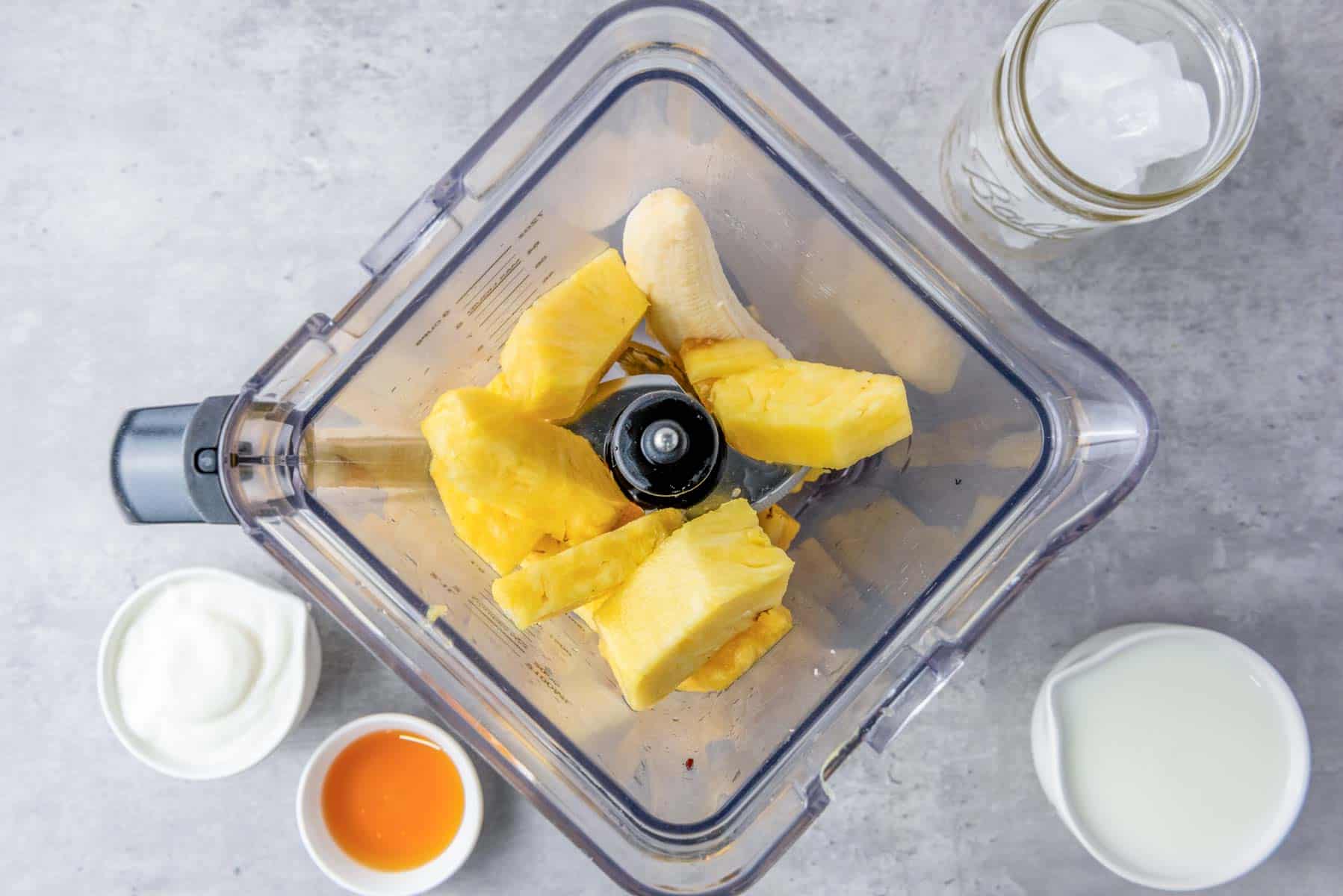 A blender with pineapple and banana as seen from overhead.