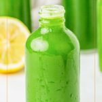 A clear bottle filled with green juice sits in front of a sliced lemon, with more bottles of green juice in the background. Text reads “Easy Green Juice” and “simplybreakfastrecipes.com”.