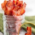A glass jar filled with strips of candied bacon, with an inset image showing a hand holding a piece, and text reading “Easy Candied Bacon.”.