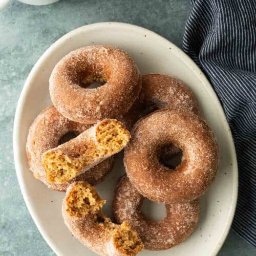 A plate of cinnamon-sugar-coated donuts, with one donut broken in half.