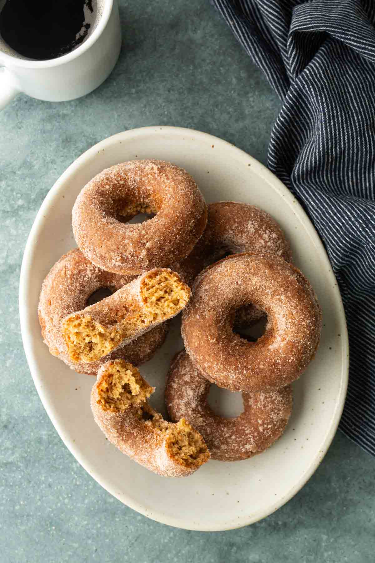 A plate of cinnamon-sugar-coated donuts, with one donut broken in half.