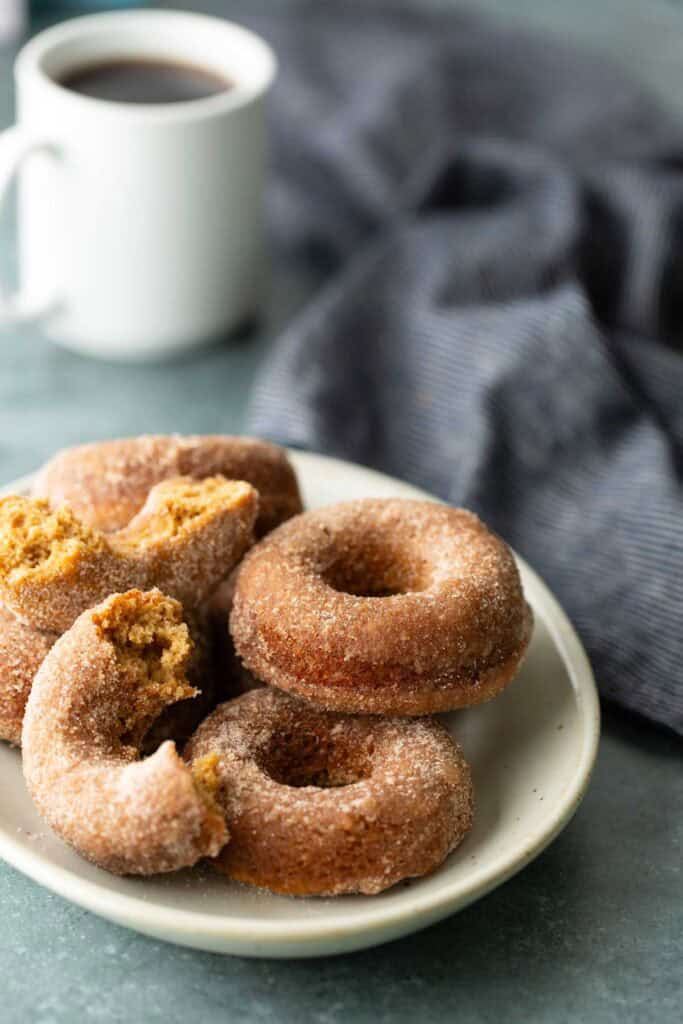 A plate of cinnamon-sugar-coated donuts, with a cup of coffee in the background.