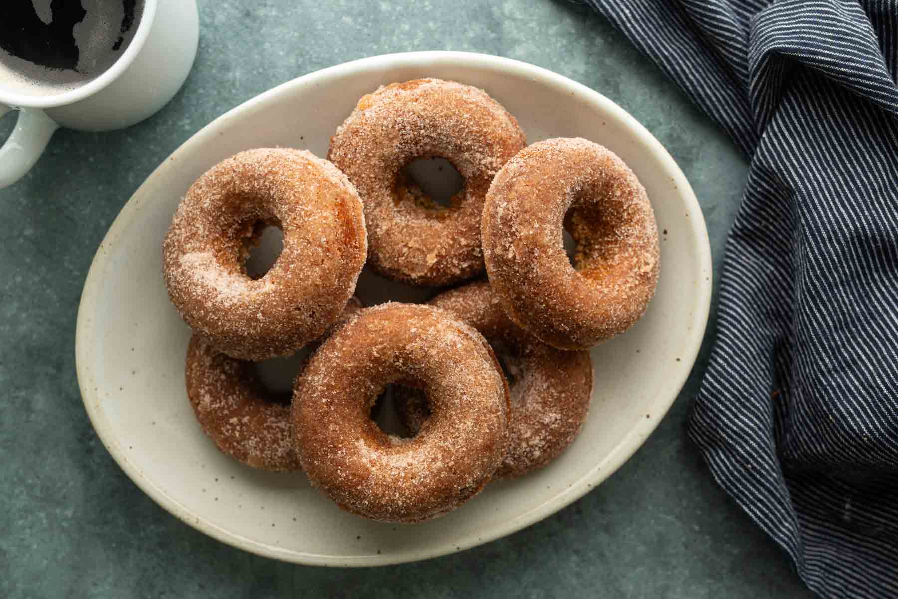A plate of six cinnamon sugar donuts next to a cup of coffee.
