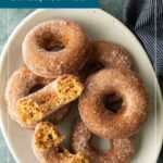 A plate of cinnamon-sugar coated apple cider donuts, with text overlay reading “APPLE CIDER DONUTS baked, not fried!” and a “READ MORE” button.